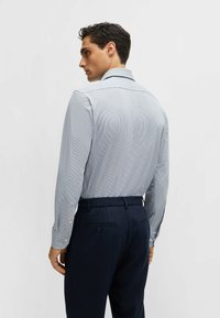 Chemise à manches longues pour homme en bleu clair avec un motif à carreaux subtil. Accompagnée de pantalons bleu marine foncé, dotés d'un bouton à la poche arrière.
