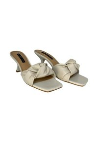 Sandali in pelle beige con un design superiore annodato, punta aperta e tacco affusolato. Scatola della punta a forma quadrata e superficie liscia.
