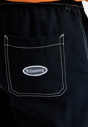 Svarta denimbyxor med en vit söm på bakfickan som har en grå oval Billabong-logotyp. Tyget har en texturerad yta.