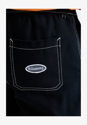 Μαύρο τζιν παντελόνι με λευκή ραφή στη πίσω τσέπη που διαθέτει το γκρι οβάλ λογότυπο της Billabong. Το ύφασμα έχει υφασμένη επιφάνεια.
