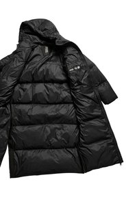 Doudoune noire avec capuche, design matelassé et texture brillante et lisse. Comprend des zips et des détails de logo sur la manche.
