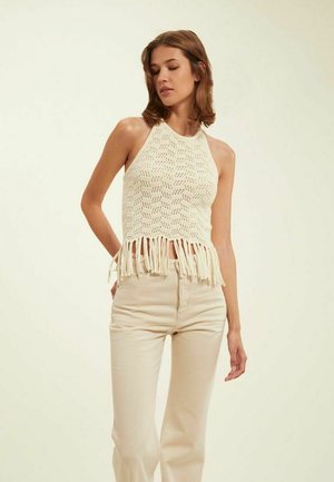 Top halter au crochet en crème avec un motif texturé et un ourlet à franges. Associé à un pantalon taille haute beige clair.