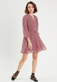 Robe portefeuille à motifs rouge et blanc avec de longues manches transparentes, une jupe fluide et un décolleté en V profond. Associée à des chaussettes noires et des chaussures.