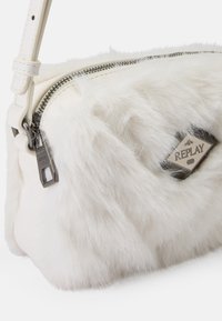 Witte nepbont schoudertas met een zilveren rits, zwarte hardware en een diamantvormig label met "REPLAY". Zachte textuur, compacte vorm.