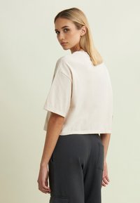 Camiseta corta de algodón de color beige claro con mangas cortas, cuello redondo y corte relajado, combinada con pantalones gris oscuro.