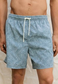 Shorts de bain à motif bleu avec un design en zigzag, dotés d'une taille élastique et d'un cordon blanc. Tissu léger avec une texture lisse.