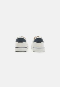 Zapatillas de lona blancas con un acento de ante azul marino en el talón, suelas de goma y una franja azul marino en contraste a lo largo de la base.