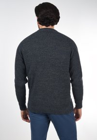 Mørkeblå teksturert strikkegenser med lange ermer og rund hals, med ribbestrikket kant og mansjetter. Båret med blå bukser.