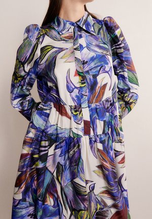 Sukienka z długim rękawem z bufkami na ramionach i kolorowym, abstrakcyjnym kwiatowym wzorem w odcieniach niebieskiego, fioletowego, zielonego i pomarańczowego na białej tkaninie.