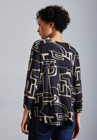 Blusa nera con un motivo geometrico beige, caratterizzata da maniche lunghe e una vestibilità morbida. Tessuto morbido, leggermente trasparente e orlo arrotondato.