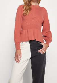 Pull en rose côtelé avec manches longues et ourlet peplum, associé à un jean bicolore : design à fente verticale noir et crème.