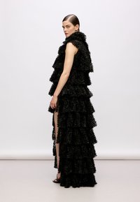 Abito nero a strati realizzato in materiale testurizzato, con ruches e uno spacco alto. Il design presenta un corpetto aderente e una gonna a strati che scende in cascata.