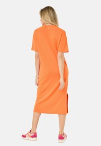 Orange t-shirtklänning i mjuk bomull, knälång med korta ärmar och sidosprund. Bärs med sneakers med rosa detaljer.
