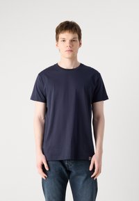 T-shirt en coton bleu marine avec un col rond et des manches courtes, arborant une petite bande rayée en bas à gauche.