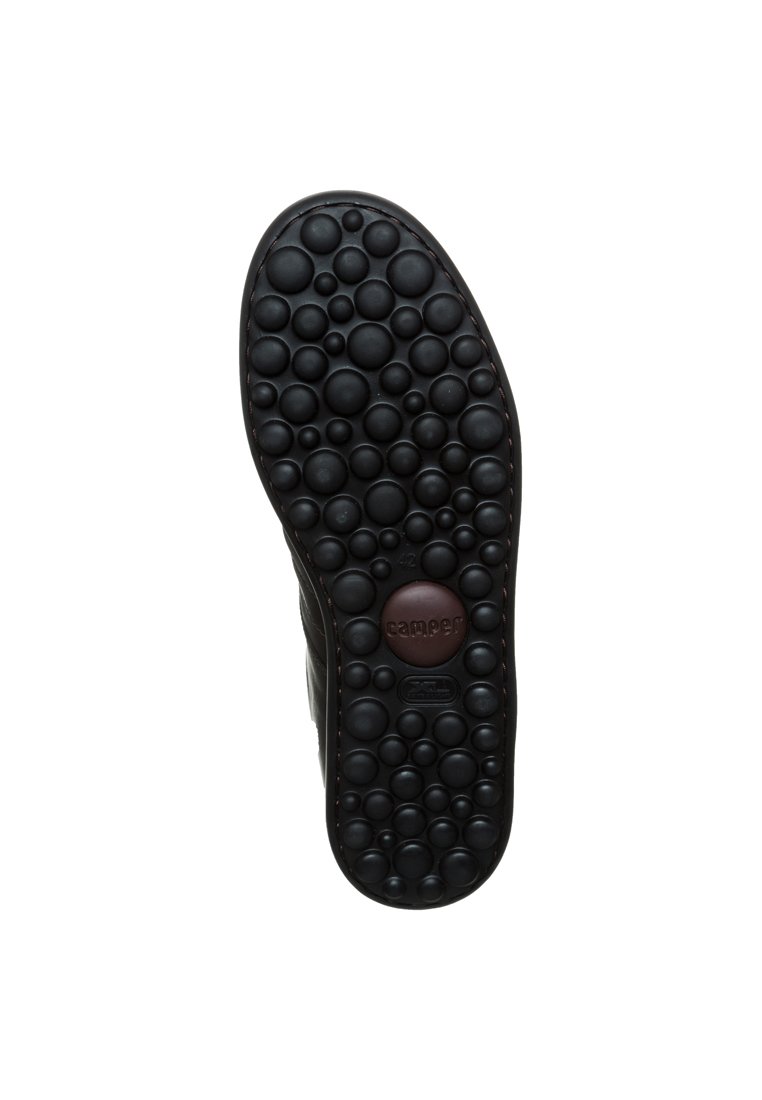 Semelle de chaussure en caoutchouc noir avec un motif de bulles texturé, présentant un disque de logo central et des bords arrondis pour une bonne adhérence et un confort optimal.