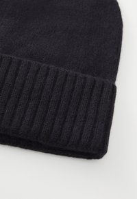 Cappello di maglia nera con risvolto a coste, posato su una superficie bianca.