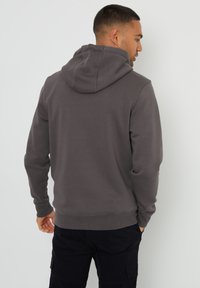 Grijze hoodie met een gladde textuur, aansluitend ontwerp en ribgebreide manchetten. De achterkant heeft een grote capuchon en een nette afwerking aan de zoom.