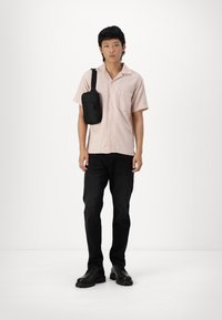 Bolso cruzado negro, camiseta de rayas rosa de manga corta, jeans negros y botas negras. Diseño sencillo con botonadura y detalle de bolsillo en el pecho.