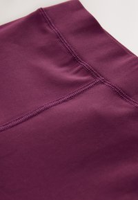 Tessuto sportivo di colore viola scuro con una texture liscia, caratterizzato da dettagli di cuciture flatlock. Il design enfatizza un aspetto senza cuciture.