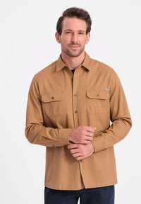 Langarm, knoopsluiting shirt van tan stof met twee borstzakken, een spitse kraag en subtiele stiksels. Draag het met een donkere denim broek.