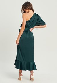 Vestido de satén verde oscuro con un diseño de un solo hombro, dobladillo acampanado y cinturón a juego en la cintura. Textura suave y caída elegante.