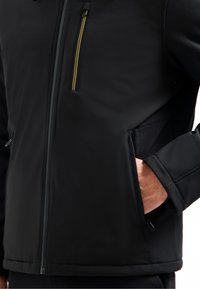 Zwarte jas van zachte stof met een ritssluiting aan de voorkant, voorzien van een gele acccent. Inclusief zijzakken en een gladde, gestructureerde afwerking.