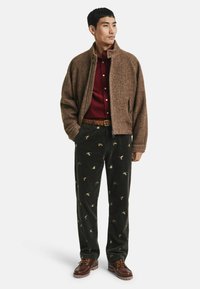 Bruine visgraatjasje, bordeaux shirt, groene corduroy broek met vogelpatronen, bruine gevlochten riem, bruine bootschoenen. Casual outfit ontwerp.