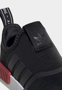 Svart sportskor med ett slankt textilöverdrag, med tre svarta ränder, en dragflik och en flerfärgad sula.