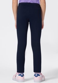 Leggings azul marino con una textura suave y una cintura elástica. Llevados con zapatos rosas de suela translúcida que presentan acentos azules.