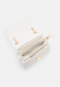 Vit läderhandväska med guldkedjestropp, öppen klaff och zipprad mittkompartment mot en vit bakgrund.