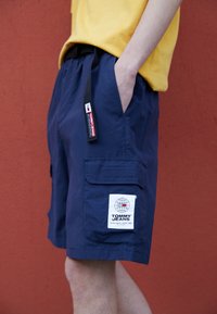 Námořnické cargo šortky s páskem a černým stahováním. Na levé noze se nachází záplata s logem. Hladká textura látky.