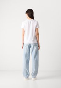 Weißes T-Shirt mit kurzen Ärmeln und leicht abgerundetem Halsausschnitt, kombiniert mit hellblauen weiten Jeans. Einfaches Design, keine Muster oder Grafiken.