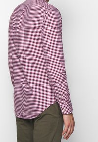 Checkered shirt in maroon and white cotton fabric; classic collar, long sleeves with button cuffs, curved hem, and back pleat detail.