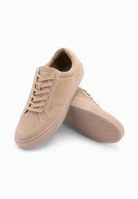 Krémové semišové tenisky s plochými tkaničkami, kulatou špičkou a gumovou podrážkou. Disponují tónovým šitím a minimální značkou na jazyku.