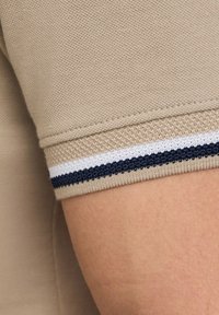 Beige polo shirt mouw met een gestructureerde stof, voorzien van een marineblauw en wit gestreepte ribbelafwerking aan de manchette. Gladde oppervlakte, casual stijl.