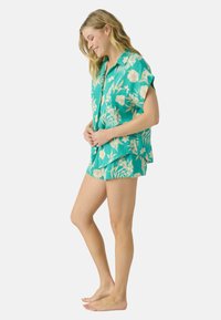 Turquoise bloemen pyjama set met een short-sleeve knoopshirt met een open kraag en bijpassende shorts. Zachte stof met een gestructureerde afwerking.