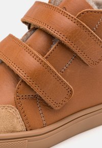 Brune lærersneaker med to Velcro-remmer, suede tåhette og en teksturert gummisåle. Sømdetaljer forbedrer designet og teksturen.