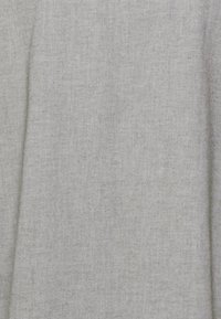 Tissu gris clair avec un tissage texturé. La surface présente des variations subtiles et des éclats, indiquant un matériau doux et respirant.