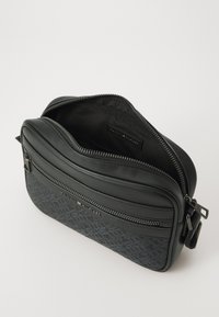 Sac en cuir noir à bandoulière avec un motif texturé, doté de deux compartiments zippés et d'accents de marque, finition lisse sur le dessus.
