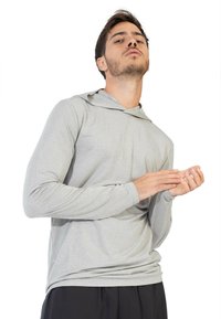 Felpa grigia chiara a maniche lunghe con un motivo testurizzato, dalla vestibilità rilassata e cappuccio integrato, indossata in modo informale sopra pantaloni scuri.