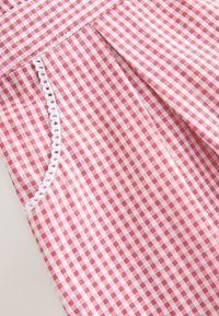 Gros plan d’un tissu vichy rose et blanc avec un pli et une bordure en dentelle blanche bouclée le long du bord.