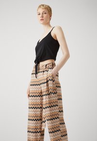 Svart avkortet tanktop med frontknute, parret med lette bukser med et ziggzag-mønster i oransje, svart og beige.