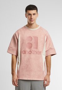 Oversized pink sweatshirt with a soft texture, features a large pink logo "another" and cream side accents, ribbed neckline.