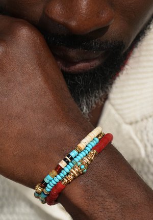 Bunte Perlenarmbänder mit Türkis-, Rot- und Cremefarbenen Perlen, akzentuiert mit goldenen Beschlägen. Das Design hat einen gestapelten Look.