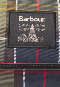 Barbour logo patch met vuurtoren en golven op een meerkleurige geruite stof met rode, blauwe, groene, gele en witte strepen.