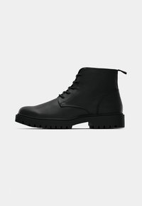 Black leather ankle boots with a rounded toe, lace-up front, and rugged rubber sole featuring deep tread for traction. Smooth texture, minimal design.