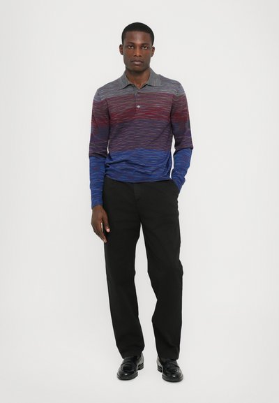 Polo de manga longa com um padrão em degradê nas tonalidades vermelho, azul e cinza; combinado com calças pretas e sapatos pretos.