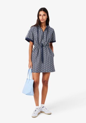 Short-sleeve navy patterned dress with a cinched waist, matching blue bag, and white sneakers. Features a hood and drawstring ties.