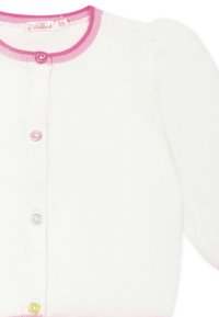 Witte gebreide cardigan met roze ribbelrand, met decoratieve knopen in roze, blauw en geel met vredesteken ontwerpen.