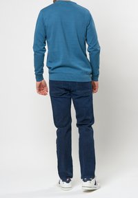 Niebieski sweter z dzianiny z okrągłym dekoltem, zestawiony z ciemnymi dżinsami. Posiada długie rękawy i ściągacze przy mankietach, uzupełniony jasnymi butami.